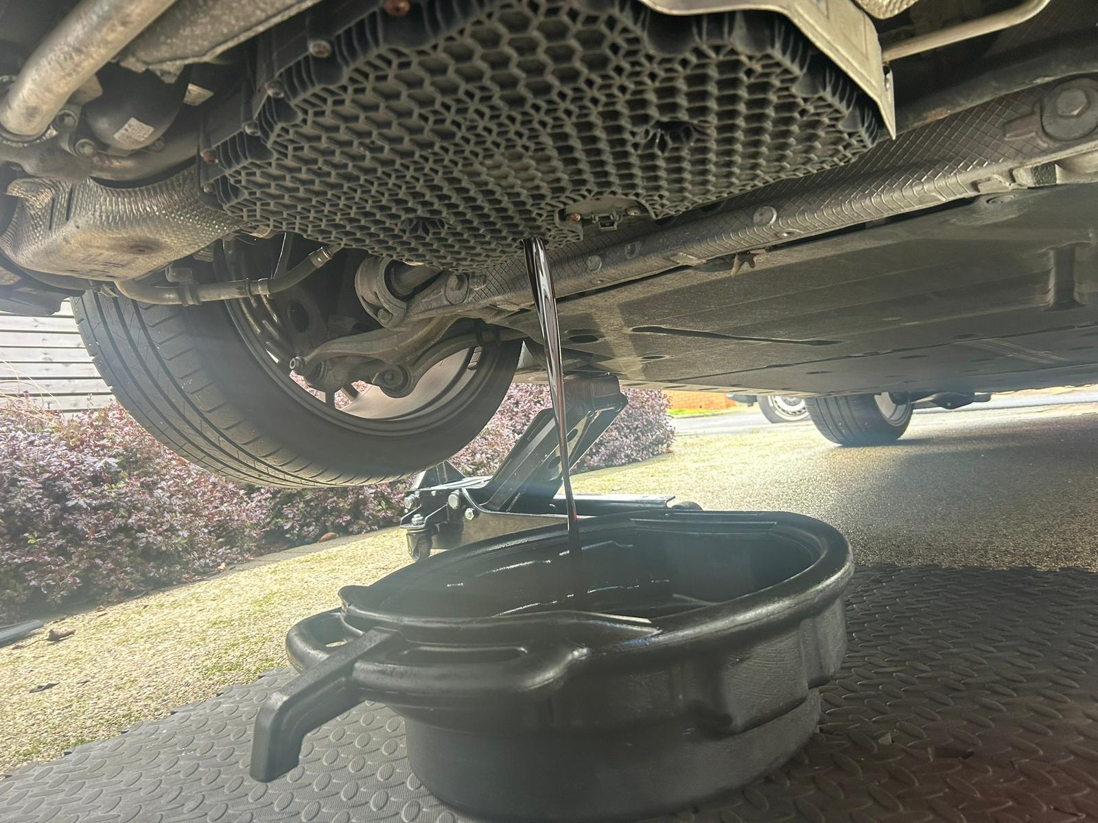Fresh oil draining from a raised vehicle into a collection pan